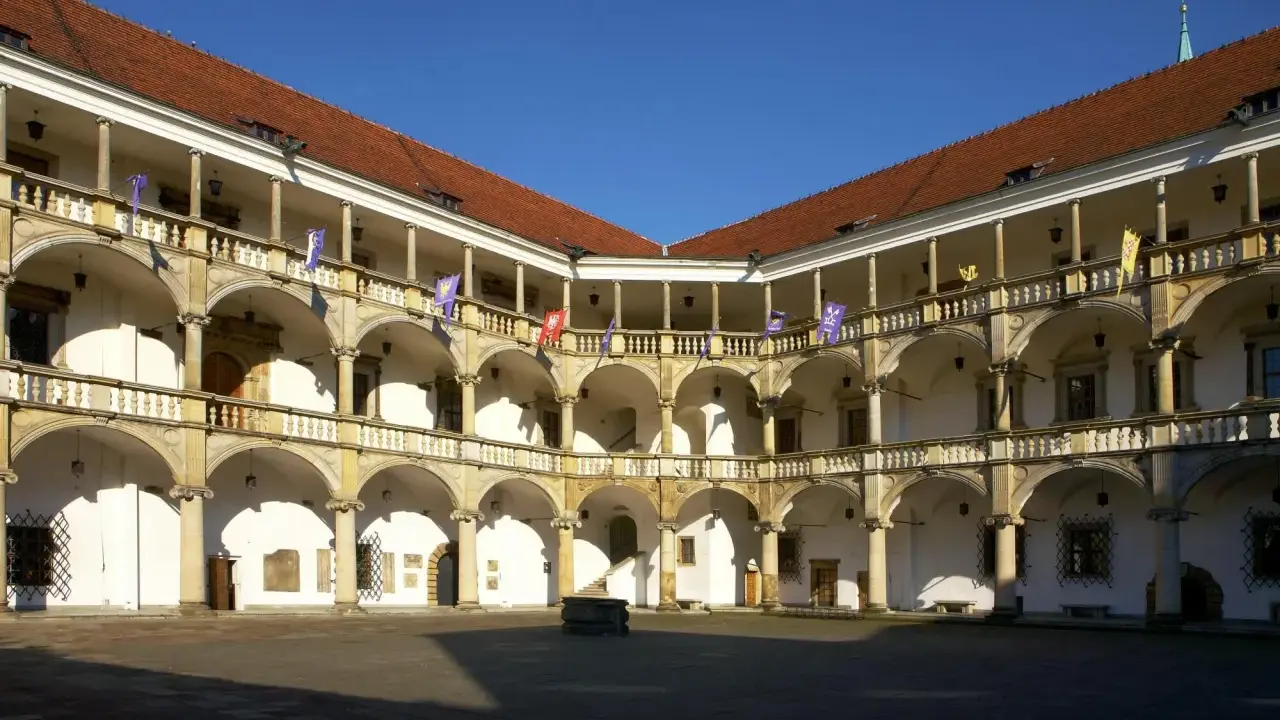 Dziedziniec zamku w Brzegu z arkadowymi krużgankami, kolumnami i flagami. Zamek w Brzegu ciekawostki – piękna renesansowa architektura.