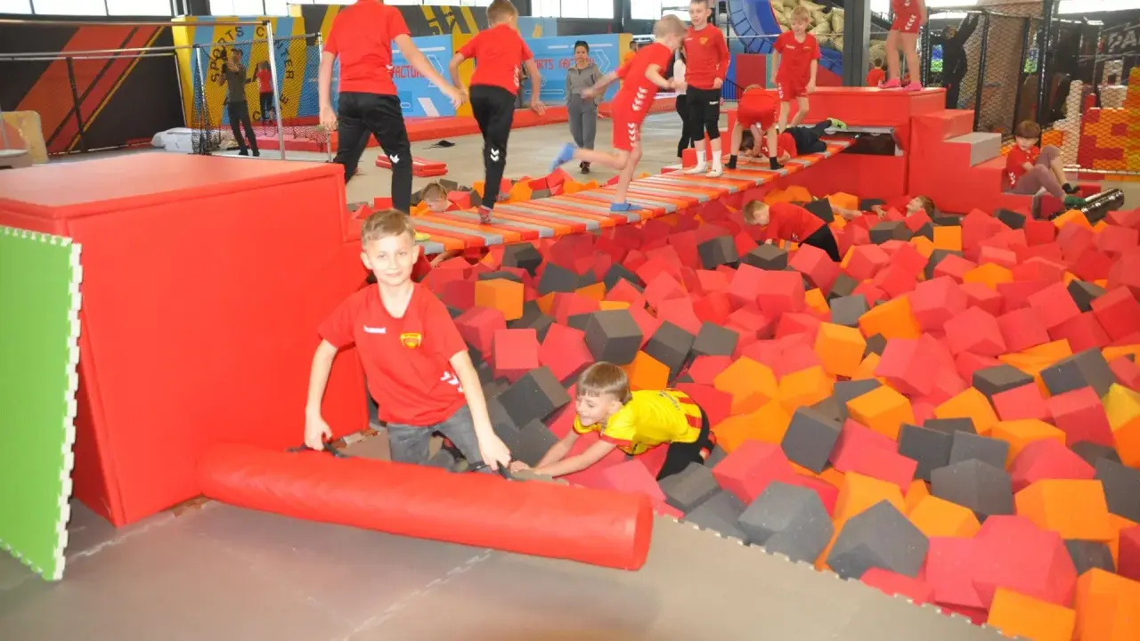 Dzieci bawią się w basenie z gąbkami w Flypark Kielce. Jeden chłopiec w czerwonej koszulce próbuje wstać, a drugi w żółtej wspina się po gąbkach.