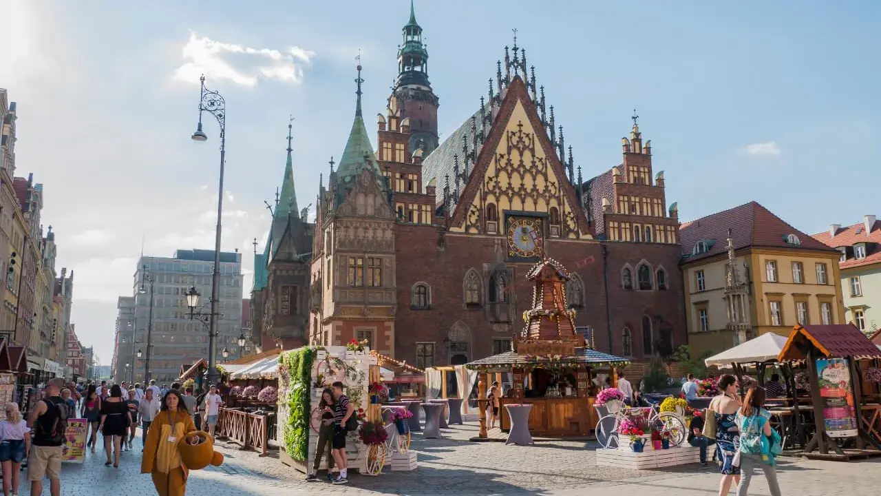 Wrocławski Rynek tętni życiem, idealne miejsce na weekendowy wypad. Ludzie spacerują, podziwiając zabytkową architekturę i kolorowe stragany.