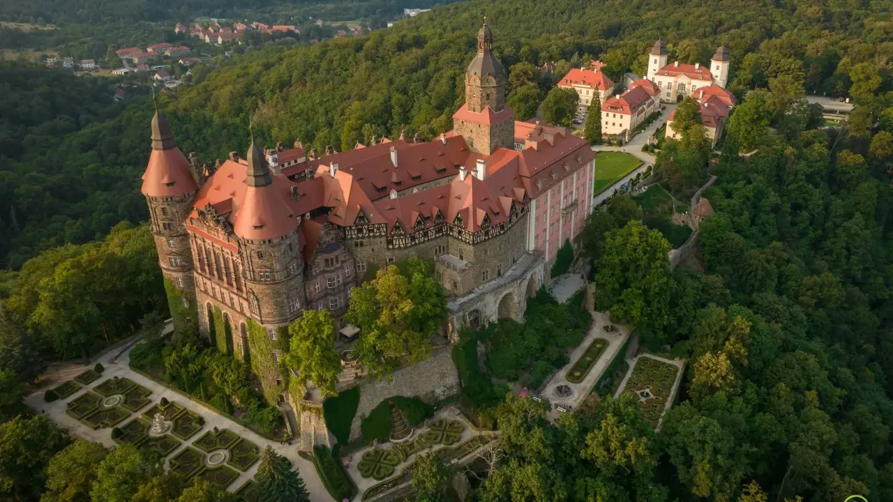 Zamek Książ otoczony zielenią, z widokiem na okoliczne wzgórza i miasteczko.