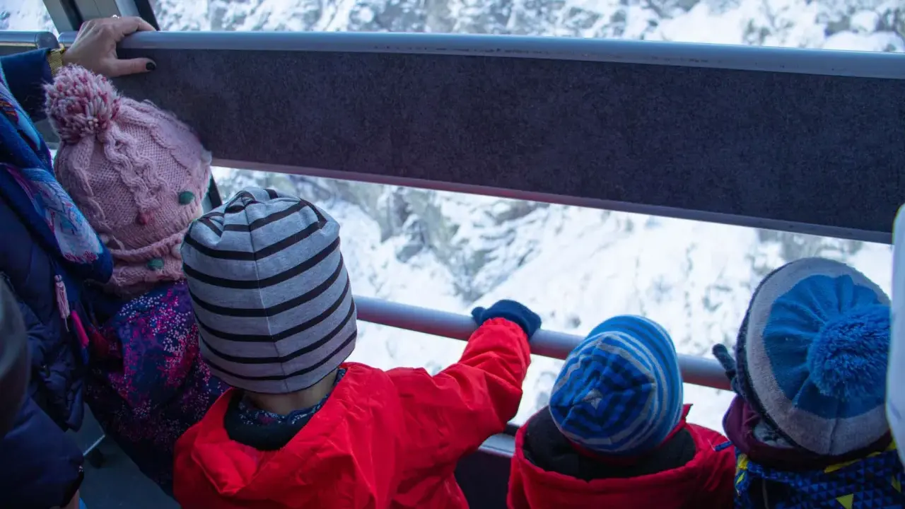 Dzieci w czapkach jadą kolejką linową na Kasprowy Wierch. Widok na ośnieżone góry.
