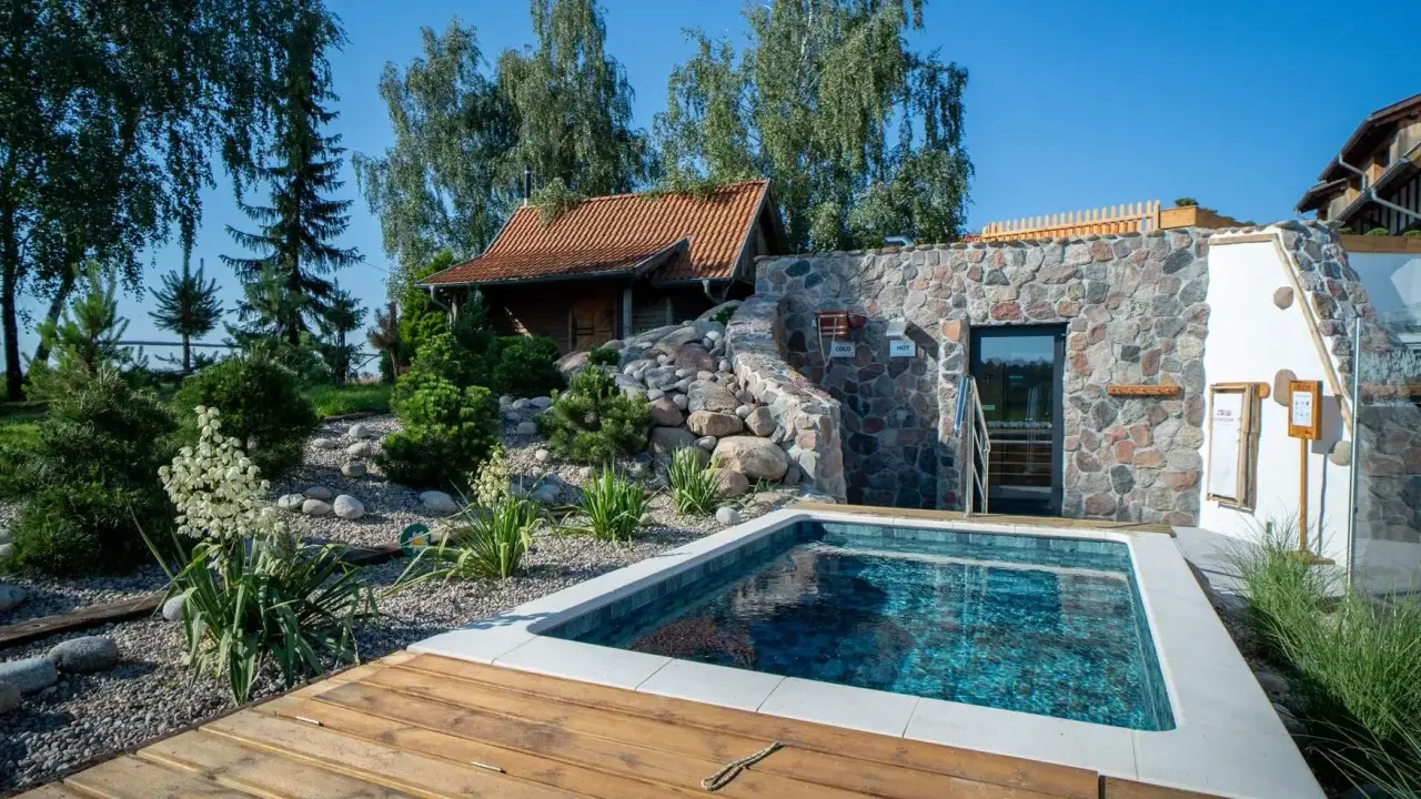Relaks w polskim spa: basenik, kamienna ściana z wejściem do sauny i urokliwy ogród. Idealne miejsce na odpoczynek.