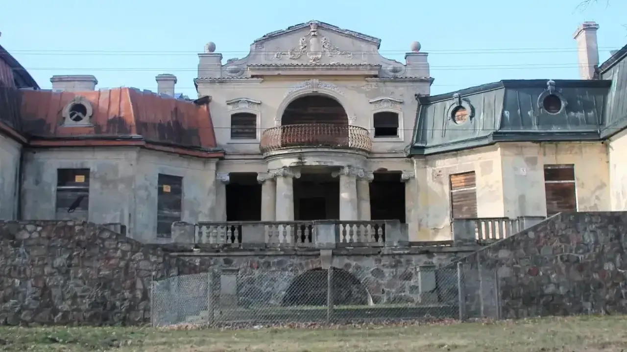 Opuszczony pałac w Bratoszewicach, zniszczony, z zabitymi deskami oknami i zardzewiałą balustradą.