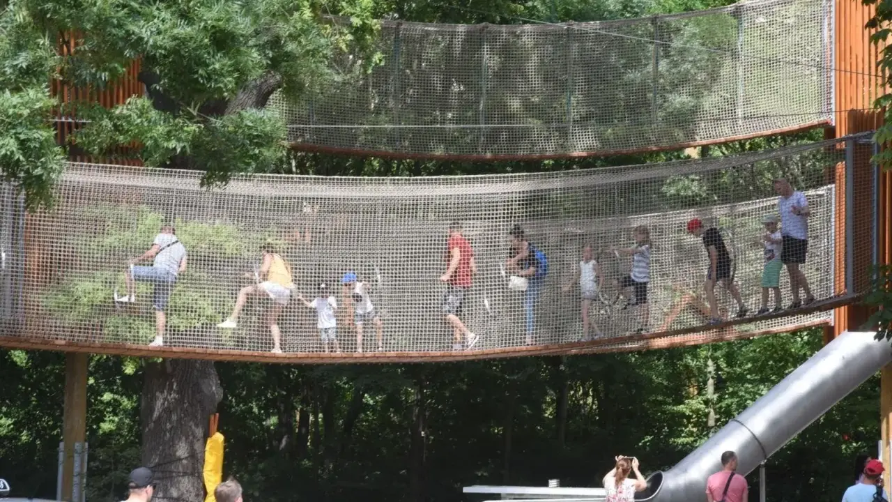 Wesoły park linowy dla dzieci z mostkami i zjeżdżalnią. Dorośli i dzieci bawią się na wysokości, ciesząc się letnim dniem.