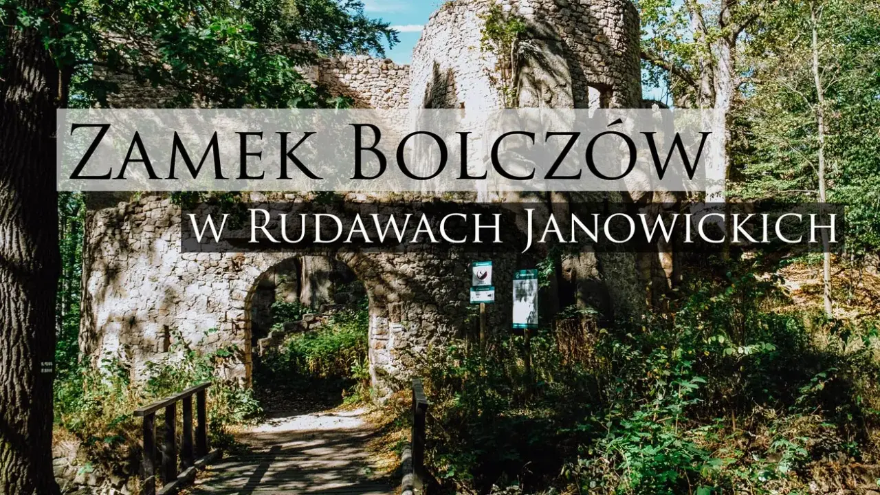 Kamienne ruiny zamku Bolczów w Rudawach Janowickich, porośnięte zielenią, z łukowym wejściem i drewnianym mostkiem.