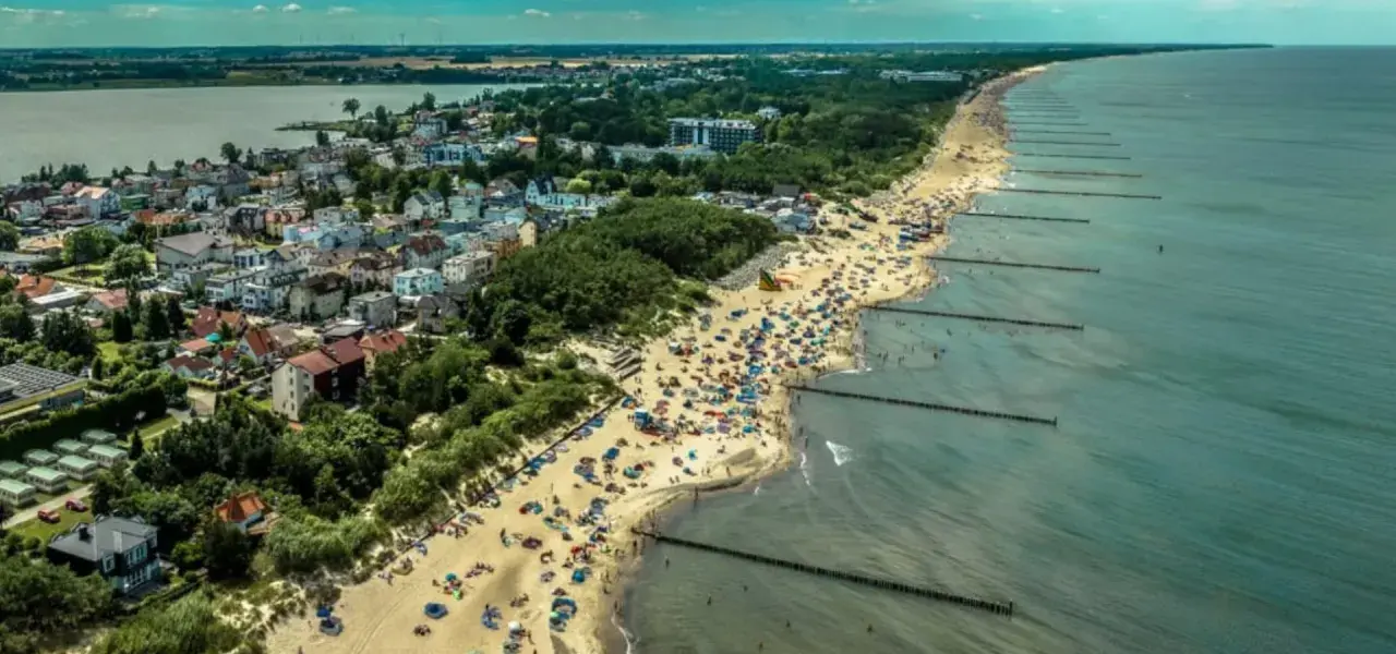 Tłum ludzi na plaży w Mielnie, cieszących się słońcem i morzem. To popularne **Mielno atrakcje** turystyczne.