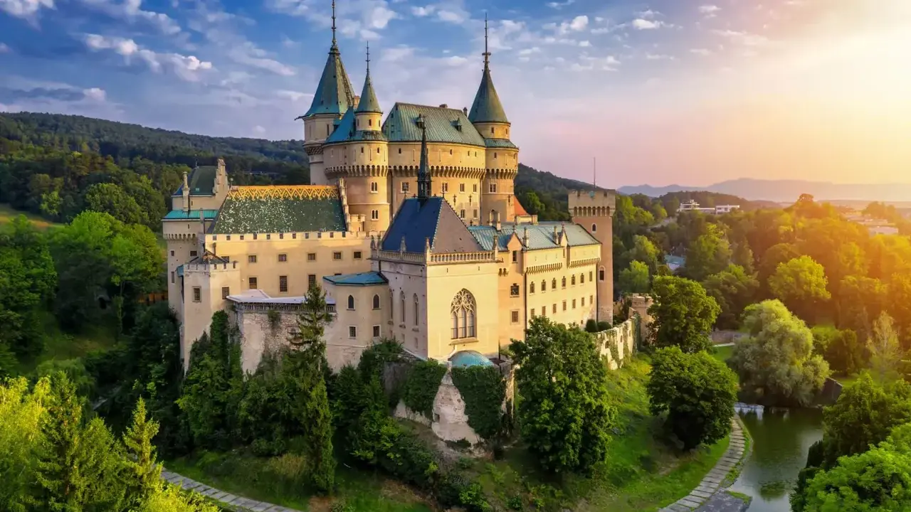 Bajkowy zamek otoczony zielenią, niczym zamek hotel w Polsce, zachwyca o zachodzie słońca.