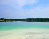 Lazurowe jezioro z piaszczystym dnem kusi do kąpieli. Piękny, spokojny krajobraz z zielonym lasem w tle.