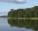 Spokojne jezioro najgłębsze w Polsce, z odbijającym się w wodzie gęstym lasem i błękitnym niebem z chmurami.