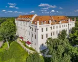 Biały zamek z czerwonym dachem, otoczony zielenią, oferuje wyjątkowe noclegi w zamkach i pałacach. Idealne miejsce na romantyczny wypad.