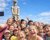 Uśmiechnięta grupa dzieci i opiekunka robią sobie selfie pod drewnianym pomnikiem. Wspaniałe kościerzyna atrakcje dla dzieci!