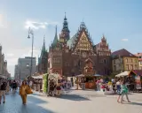 Wrocławski Rynek tętni życiem, idealne miejsce na weekendowy wypad. Ludzie spacerują, podziwiając zabytkową architekturę i kolorowe stragany.