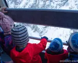 Dzieci w czapkach jadą kolejką linową na Kasprowy Wierch. Widok na ośnieżone góry.