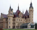 Zamek Książ, jeden z najpiękniejszych zamków w Polsce, z charakterystycznymi wieżami i czerwonymi dachami, otoczony zielenią.
