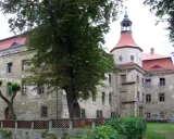 Zamek w Domanicach, zniszczony, z czerwoną dachem i wieżą, otoczony zielenią.
