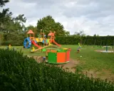 Kolorowy plac zabaw z karuzelą i huśtawkami, idealny dla dzieci odwiedzających farmę strusi Kniewo.