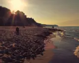 Zachód słońca nad morzem w Chłapowie. Piasek, fale i spacerujący ludzie wzdłuż klifu.