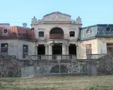 Opuszczony pałac w Bratoszewicach, zniszczony, z zabitymi deskami oknami i zardzewiałą balustradą.