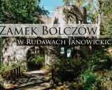 Kamienne ruiny zamku Bolczów w Rudawach Janowickich, porośnięte zielenią, z łukowym wejściem i drewnianym mostkiem.