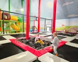 Dzieci bawią się w sławutówko park ewolucji, skacząc na trampolinach i w basenie z gąbkami. Kolorowe zjeżdżalnie i ściany z motywami zwierząt tworzą radosną atmosferę.