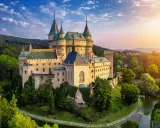 Bajkowy zamek otoczony zielenią, niczym zamek hotel w Polsce, zachwyca o zachodzie słońca.