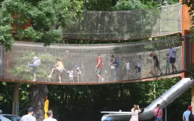 Wesoły park linowy dla dzieci z mostkami i zjeżdżalnią. Dorośli i dzieci bawią się na wysokości, ciesząc się letnim dniem.