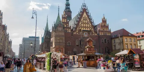 Wrocławski Rynek tętni życiem, idealne miejsce na weekendowy wypad. Ludzie spacerują, podziwiając zabytkową architekturę i kolorowe stragany.