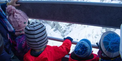 Dzieci w czapkach jadą kolejką linową na Kasprowy Wierch. Widok na ośnieżone góry.
