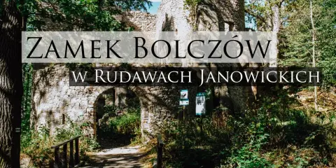 Kamienne ruiny zamku Bolczów w Rudawach Janowickich, porośnięte zielenią, z łukowym wejściem i drewnianym mostkiem.