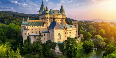 Bajkowy zamek otoczony zielenią, niczym zamek hotel w Polsce, zachwyca o zachodzie słońca.