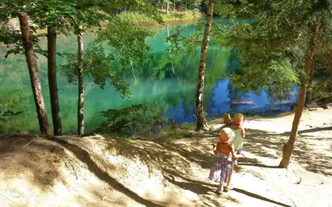 Dwie dziewczynki w słomkowych kapeluszach idą ścieżką nad turkusowe jezioro. Idealne miejsce, gdzie w góry z dzieckiem na spacer.