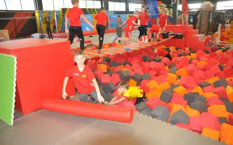 Dzieci bawią się w basenie z gąbkami w Flypark Kielce. Jeden chłopiec w czerwonej koszulce próbuje wstać, a drugi w żółtej wspina się po gąbkach.