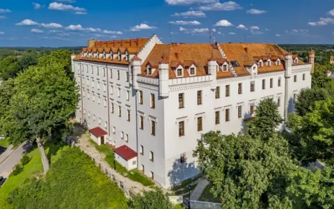 Biały zamek z czerwonym dachem, otoczony zielenią, oferuje wyjątkowe noclegi w zamkach i pałacach. Idealne miejsce na romantyczny wypad.