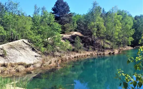 Turkusowe jezioro otoczone lasem, z piaszczystym zboczem. Wygląda jak łuk Mużakowa z kosmosu.