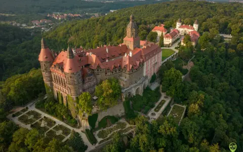 Zamek Książ otoczony zielenią, z widokiem na okoliczne wzgórza i miasteczko.