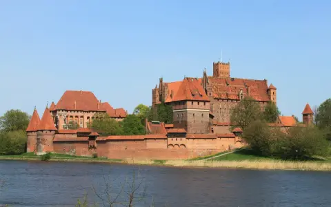 Potężne ceglane zamki na Mazurach, z czerwonymi dachami i wieżami, górują nad spokojną wodą.