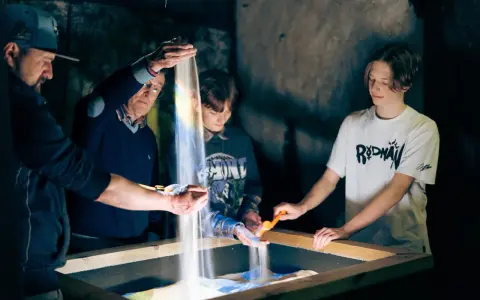 Rodzina tworzy piaskowe obrazy, świetna zabawa, gdy pada deszcz. Małopolska oferuje takie atrakcje.