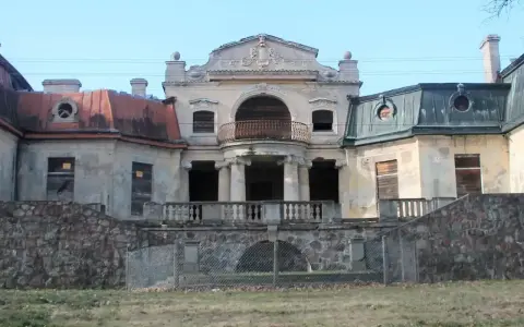 Opuszczony pałac w Bratoszewicach, zniszczony, z zabitymi deskami oknami i zardzewiałą balustradą.
