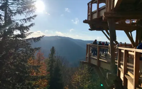 Rodzina podziwia jesienne **Beskidy z dzieckiem** na drewnianej wieży widokowej. Słońce przebija się przez drzewa.