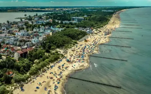 Tłum ludzi na plaży w Mielnie, cieszących się słońcem i morzem. To popularne **Mielno atrakcje** turystyczne.