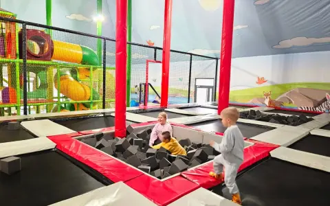 Dzieci bawią się w sławutówko park ewolucji, skacząc na trampolinach i w basenie z gąbkami. Kolorowe zjeżdżalnie i ściany z motywami zwierząt tworzą radosną atmosferę.