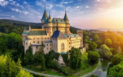 Bajkowy zamek otoczony zielenią, niczym zamek hotel w Polsce, zachwyca o zachodzie słońca.
