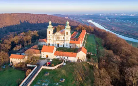 Wielki klasztor na wzgórzu, niczym milczący zakonnik, wita pierwsze promienie słońca. Obok rzeka i miasto w oddali.