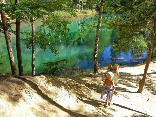 Dwie dziewczynki w słomkowych kapeluszach idą ścieżką nad turkusowe jezioro. Idealne miejsce, gdzie w góry z dzieckiem na spacer.