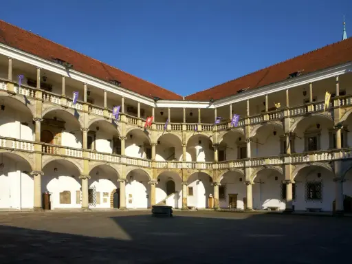 Dziedziniec zamku w Brzegu z arkadowymi krużgankami, kolumnami i flagami. Zamek w Brzegu ciekawostki – piękna renesansowa architektura.