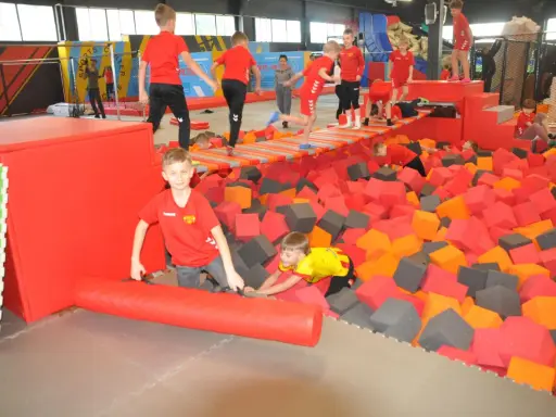 Dzieci bawią się w basenie z gąbkami w Flypark Kielce. Jeden chłopiec w czerwonej koszulce próbuje wstać, a drugi w żółtej wspina się po gąbkach.
