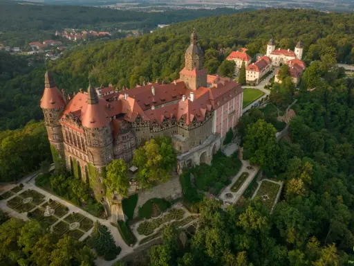 Zamek Książ otoczony zielenią, z widokiem na okoliczne wzgórza i miasteczko.