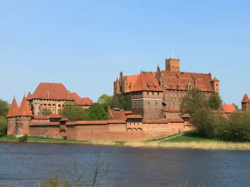 Potężne ceglane zamki na Mazurach, z czerwonymi dachami i wieżami, górują nad spokojną wodą.
