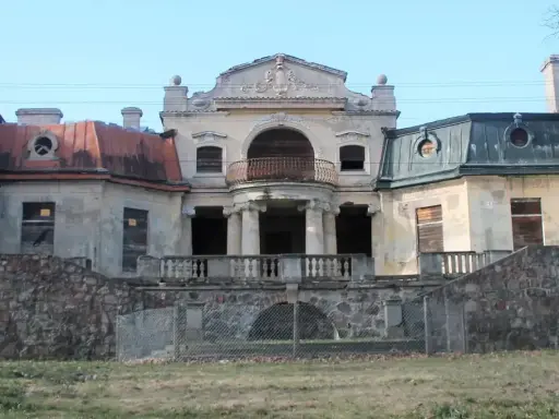 Opuszczony pałac w Bratoszewicach, zniszczony, z zabitymi deskami oknami i zardzewiałą balustradą.