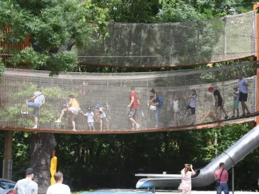 Wesoły park linowy dla dzieci z mostkami i zjeżdżalnią. Dorośli i dzieci bawią się na wysokości, ciesząc się letnim dniem.